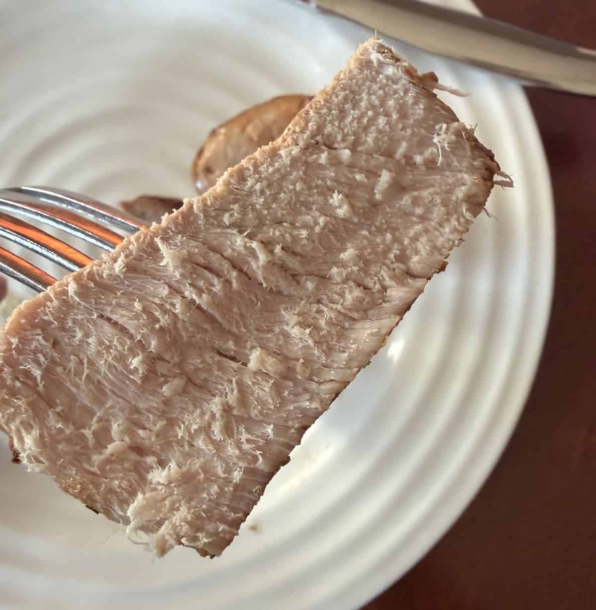Closeup image of one piece of pork tenderloin on a fork close to the camera.
