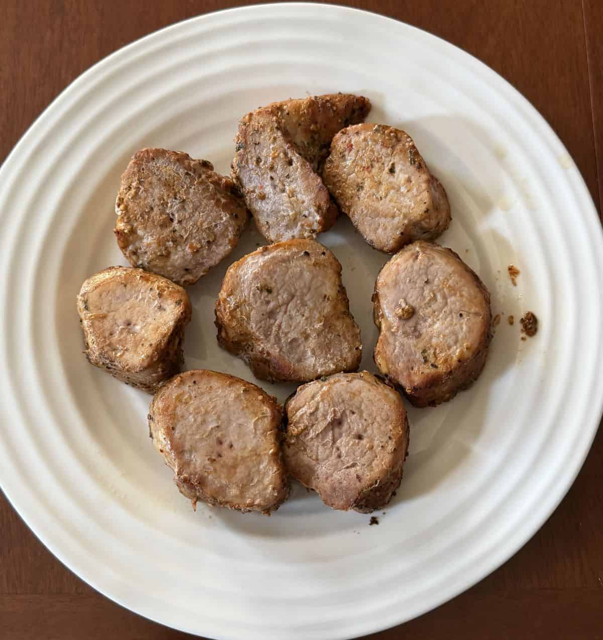 Top down image of the pork medallions served on a white plate after being cooked.