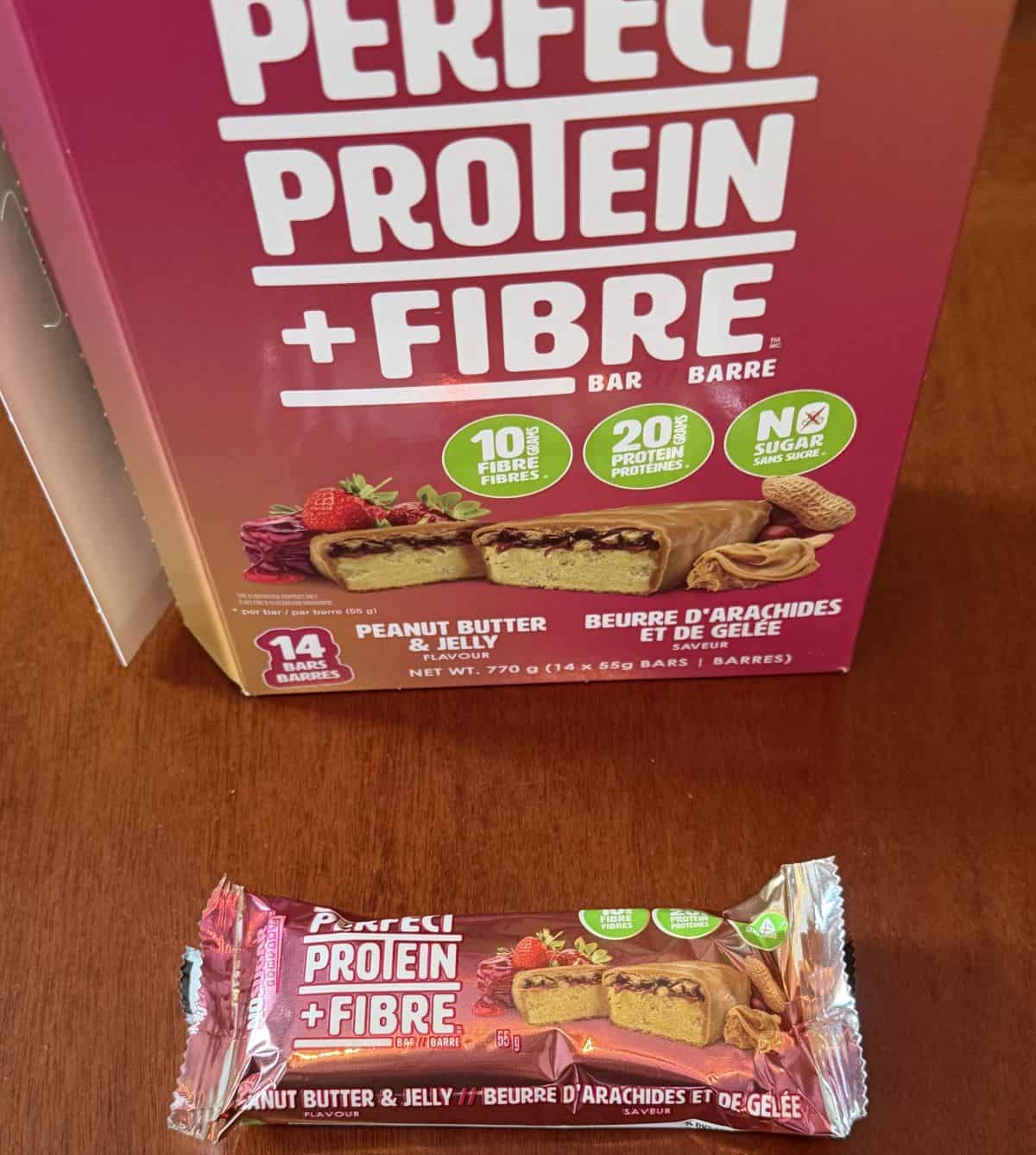 Image of one individually wrapped protein bar sitting on a table in front of the box of protein bars.