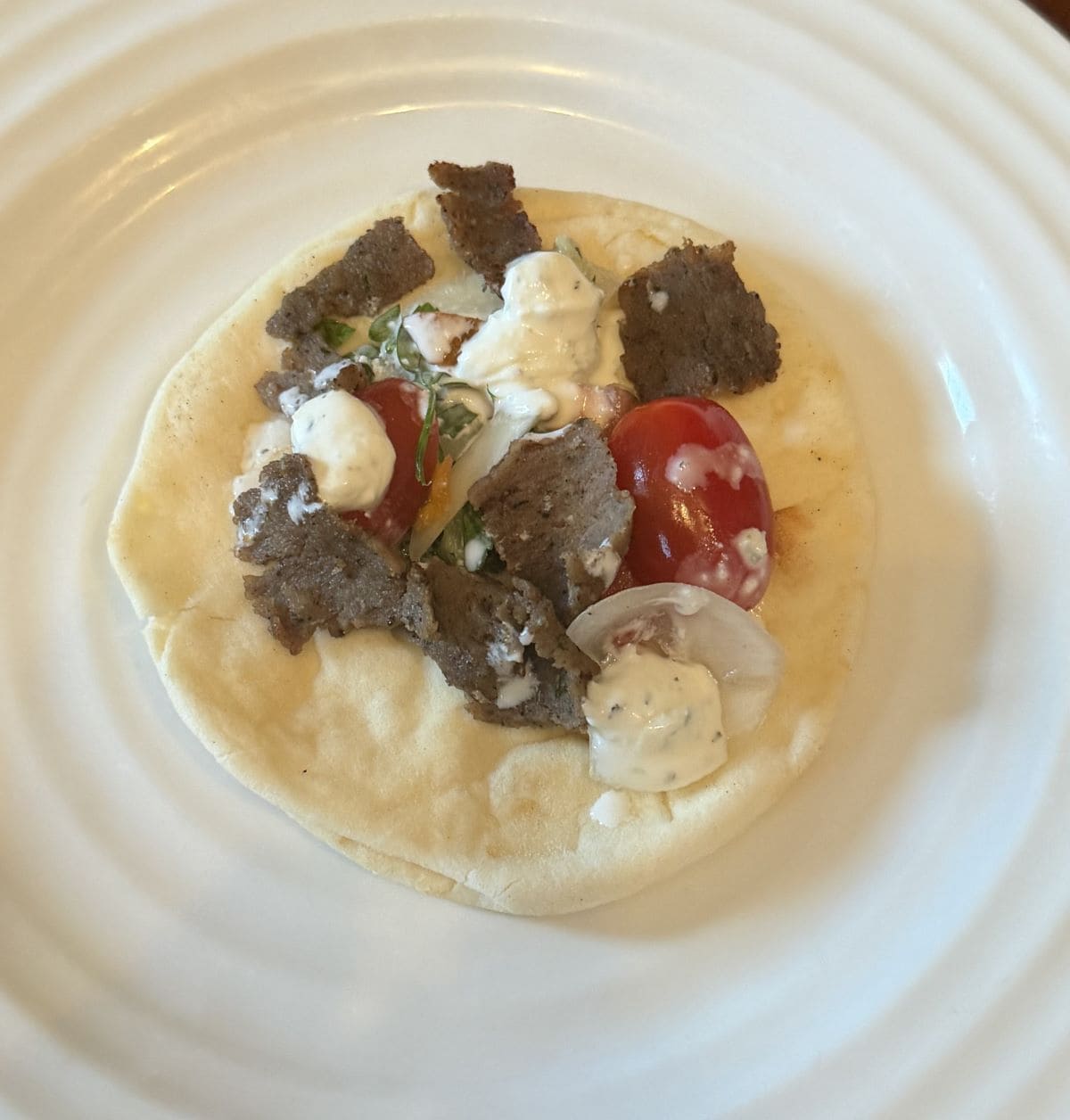 Top down image of one Gyro Pita open faced served on a white plate with tomatoes and tzatziki.