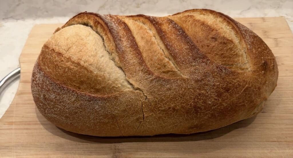 Image of a whole Kirkland Signature Italian Rustic Loaf before being cut served on a wooden cutting board.