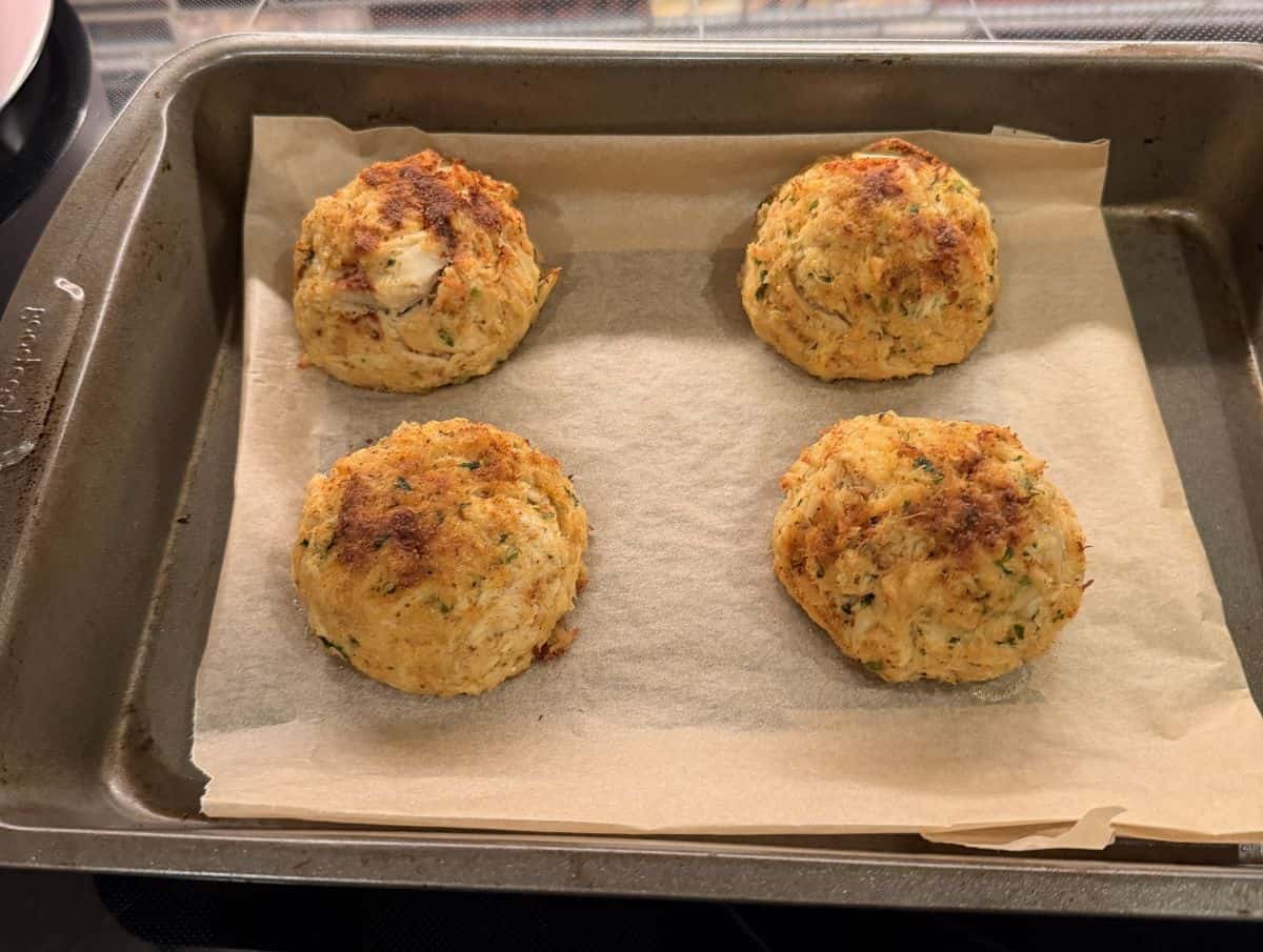 Image of four crab cakes on a baking tray after being heated in the oven.