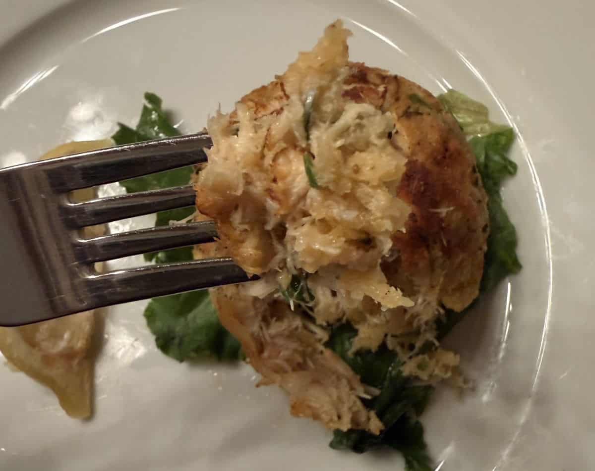 Image of one crab cake close to the camera with a fork taking a bite out of the crab cake.