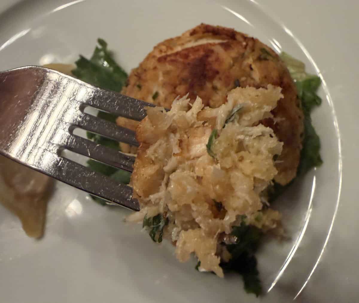 Top down closeup image of a crab cake with a fork going into it showing what the inside looks like.