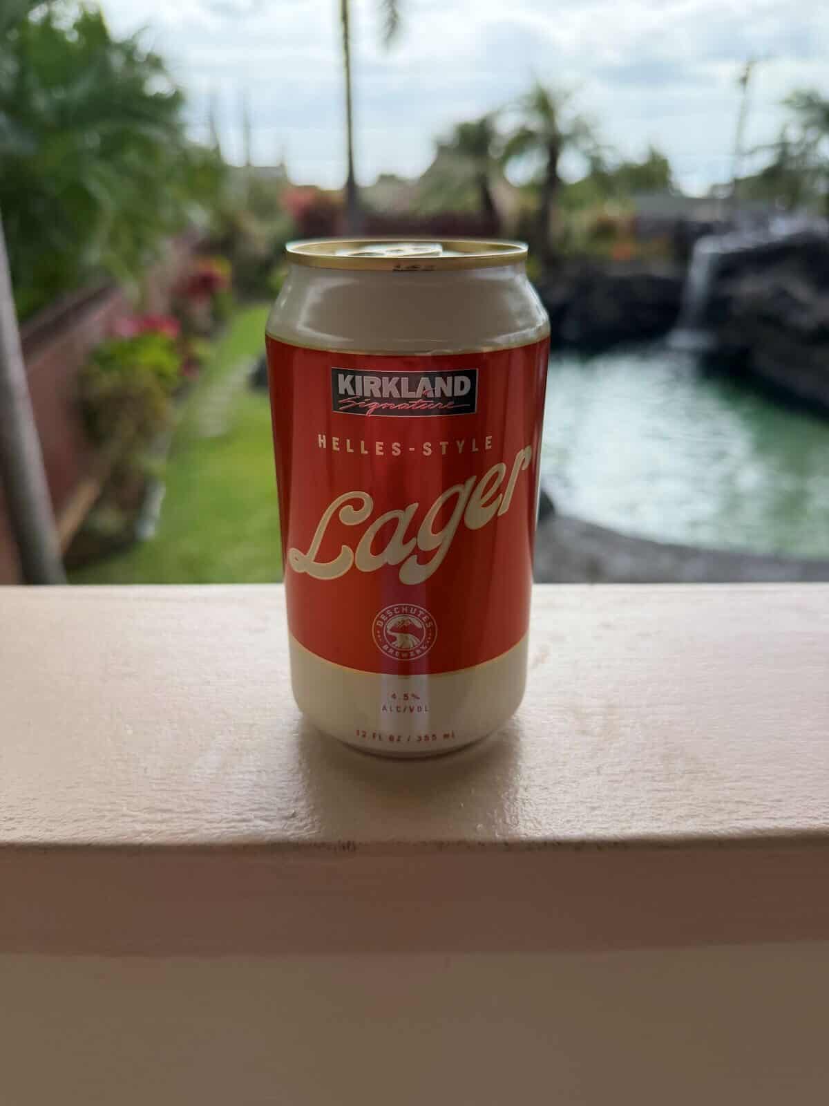 Image of a can of beer on a deck, in the background is a pool and palm trees,