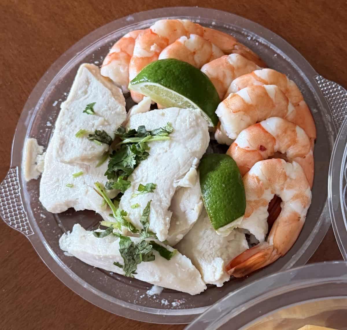 Top down image of the tray that contains shrimp, chicken, lime and cilantro.