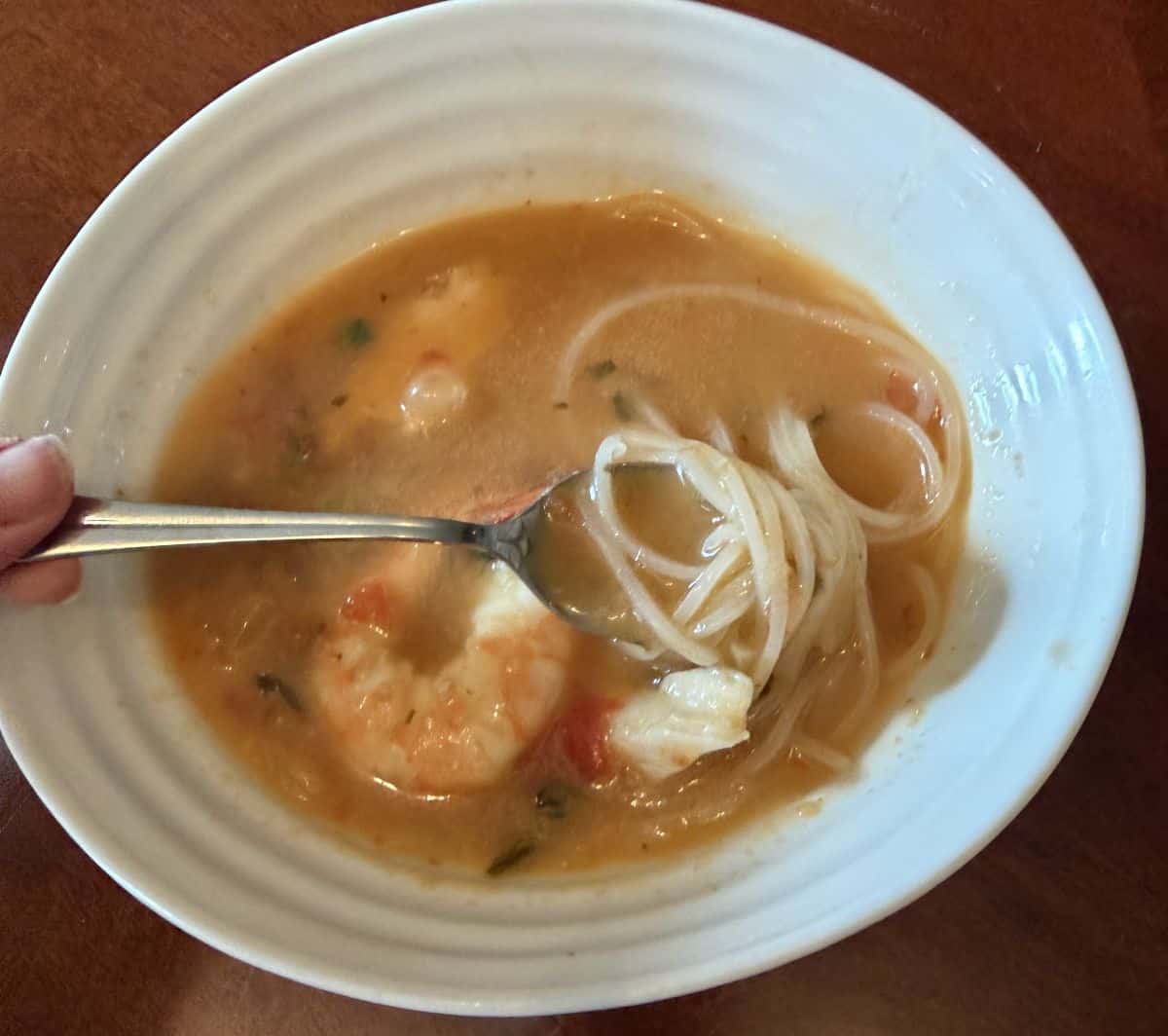 Image of a bowl of the Tom Yum Soup with shrimp and noodles and chicken in it.