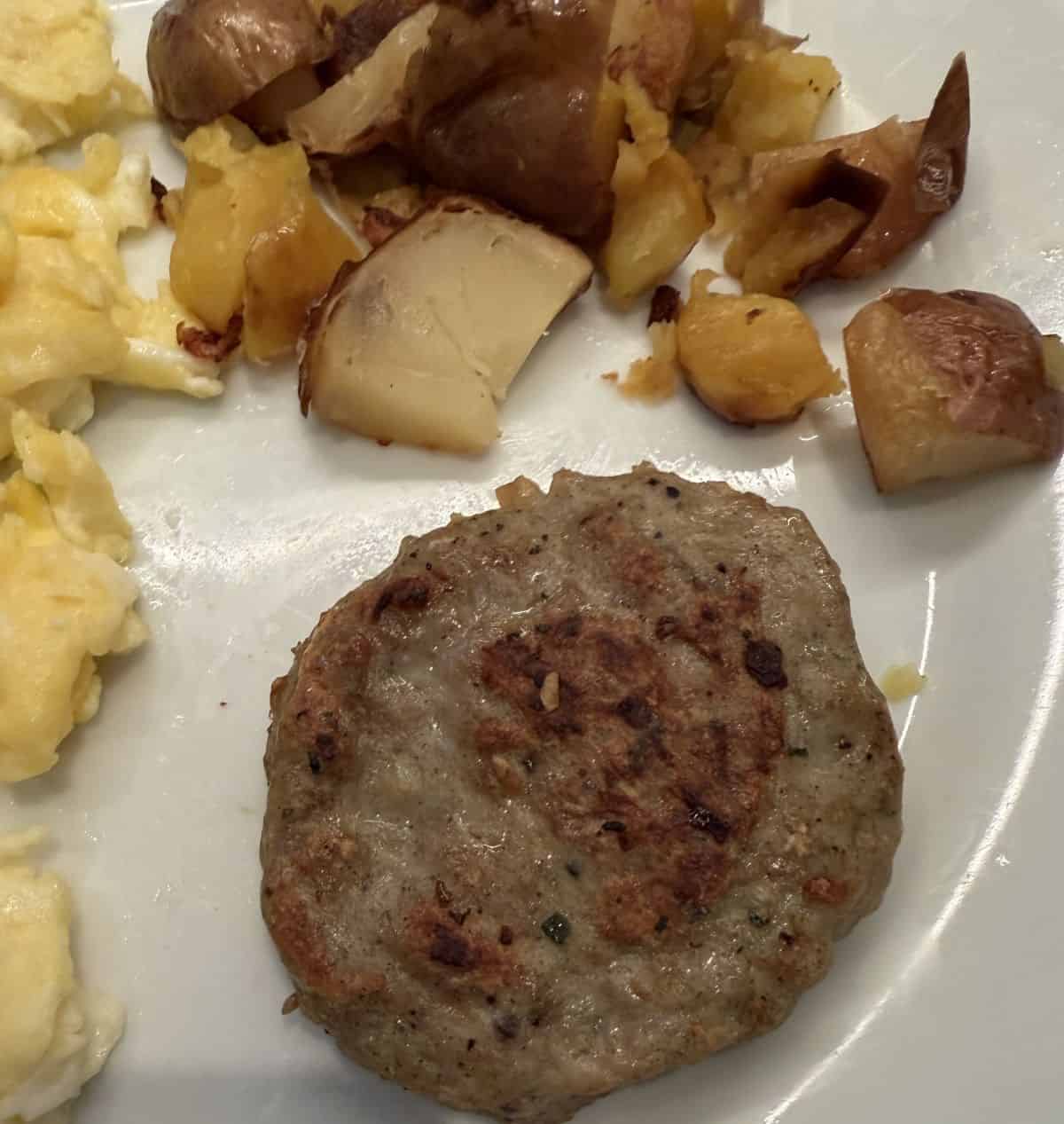 Top down image of one cooked chicken patty served on a white plate beside eggs and potatoes.