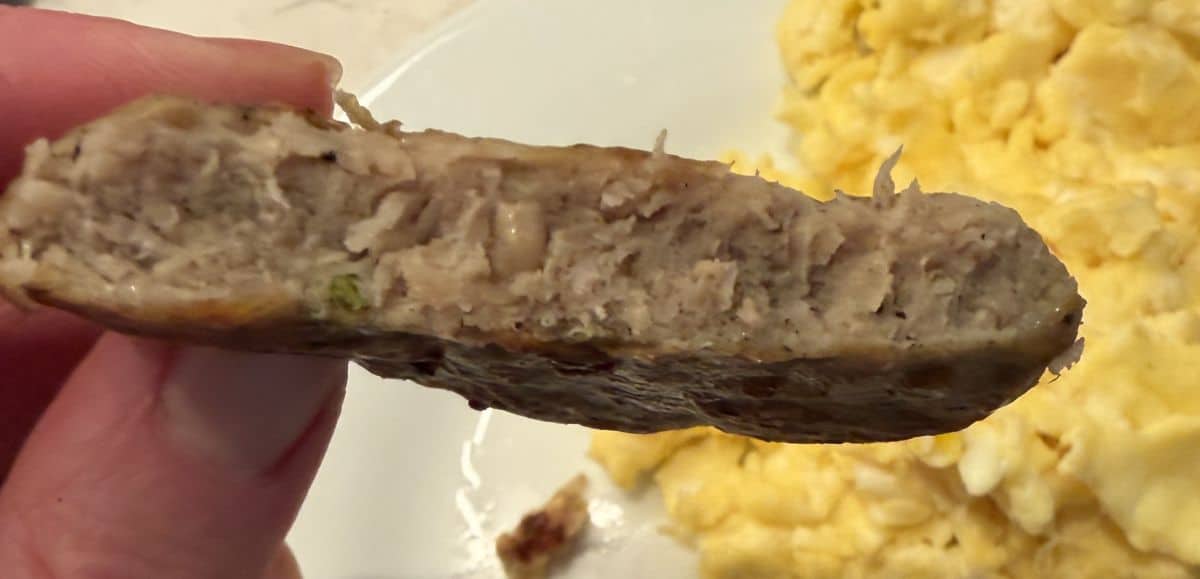Image of a hand holding a chicken patty close to the camera that's been cut in half so you can see the center of the patty.