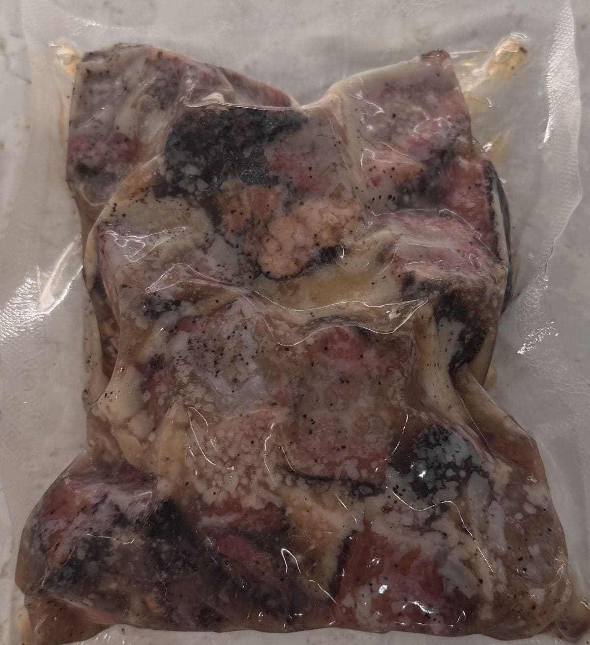 Image of one vacuum-sealed pack of unheated burnt ends sitting on a counter unopened.