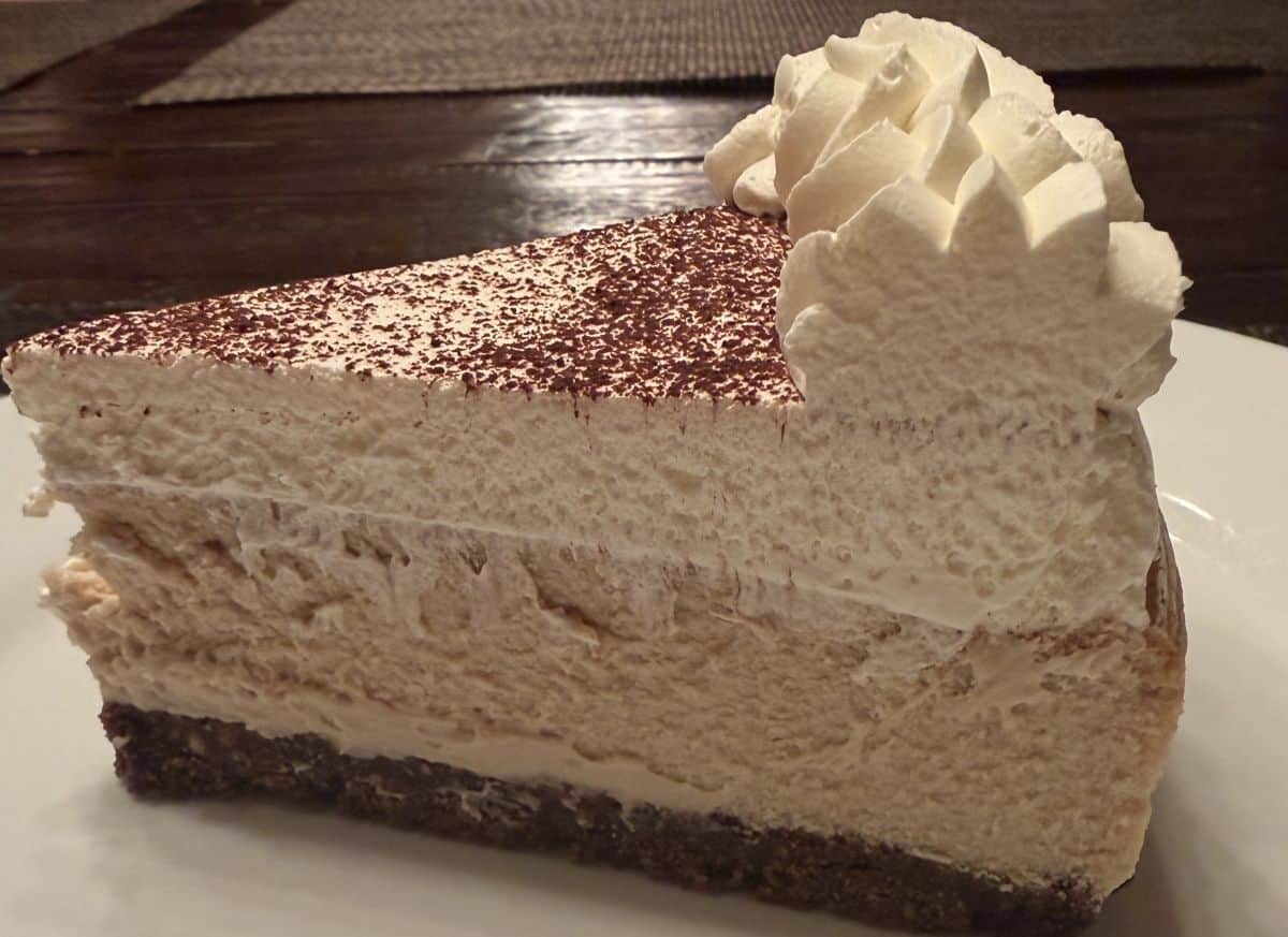 Closeup image of one slice of cheesecake served on a white plate, you can see all the different layers in the cheesecake.