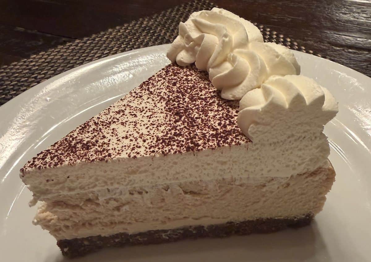 Sideview image of one slice of cheesecake served on a white plate.