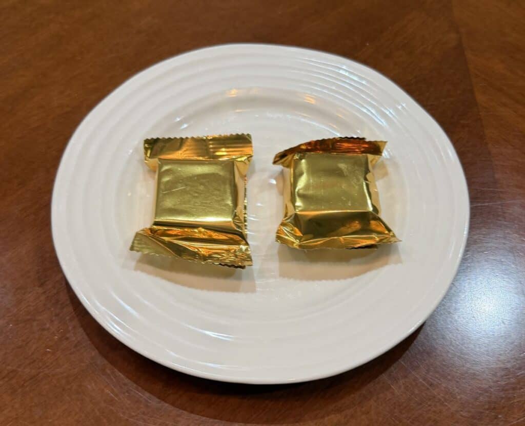 Image of two individually wrapped chocolates unopened served on a white plate.