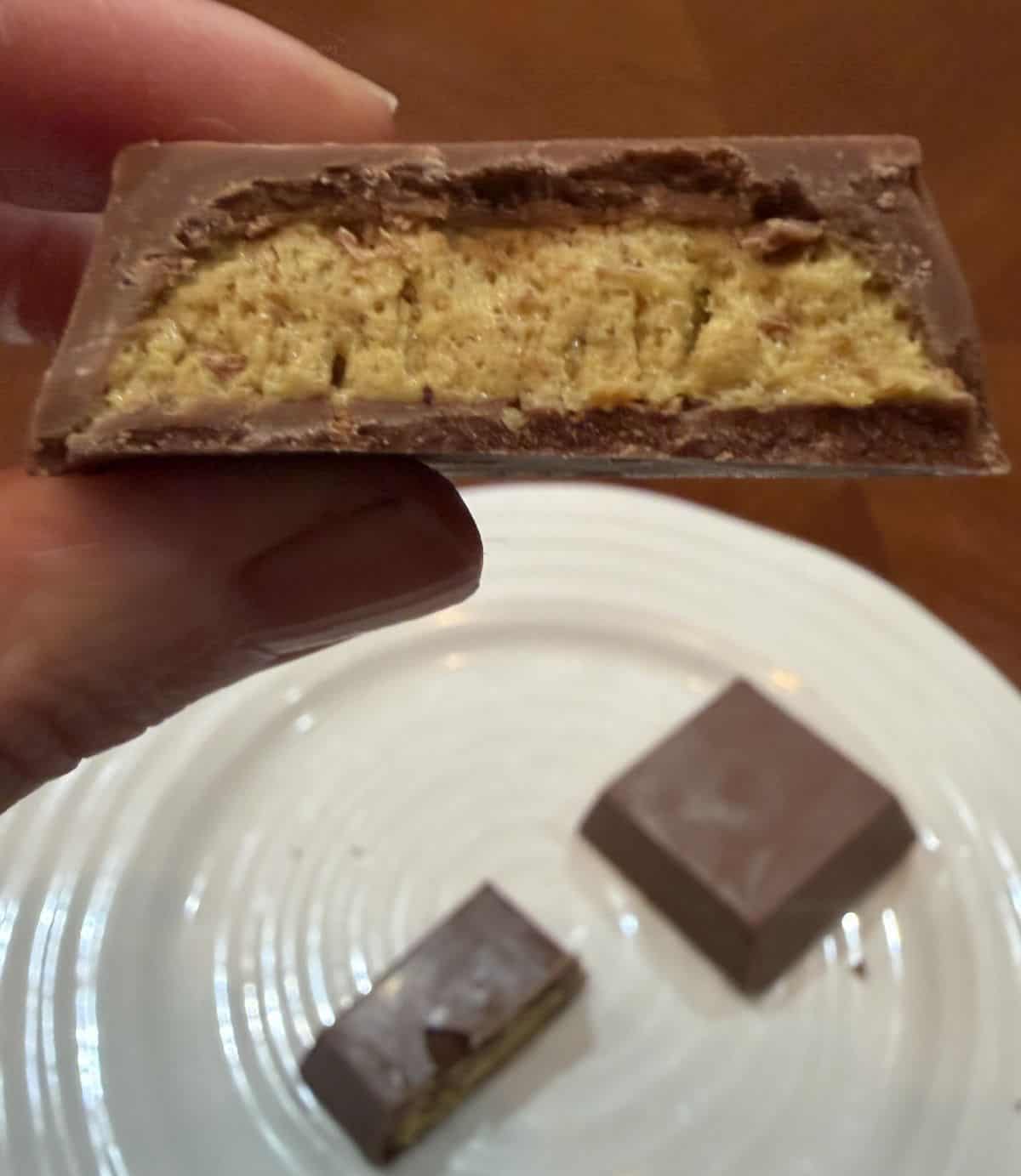Image of a hand holding one Dubai style chocolate close to the camera that's been cut in half so you can see the center.