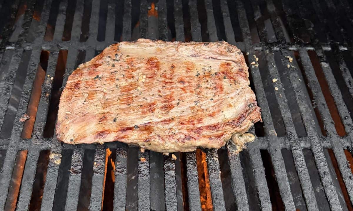 Image of the steak cooking on a grill outside.