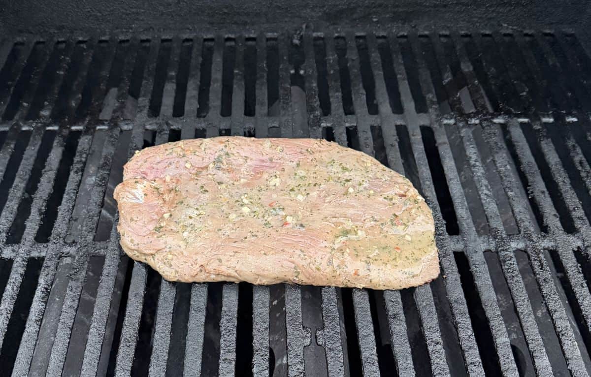 Image of a steak with marinade on it cooking on a grill outside.