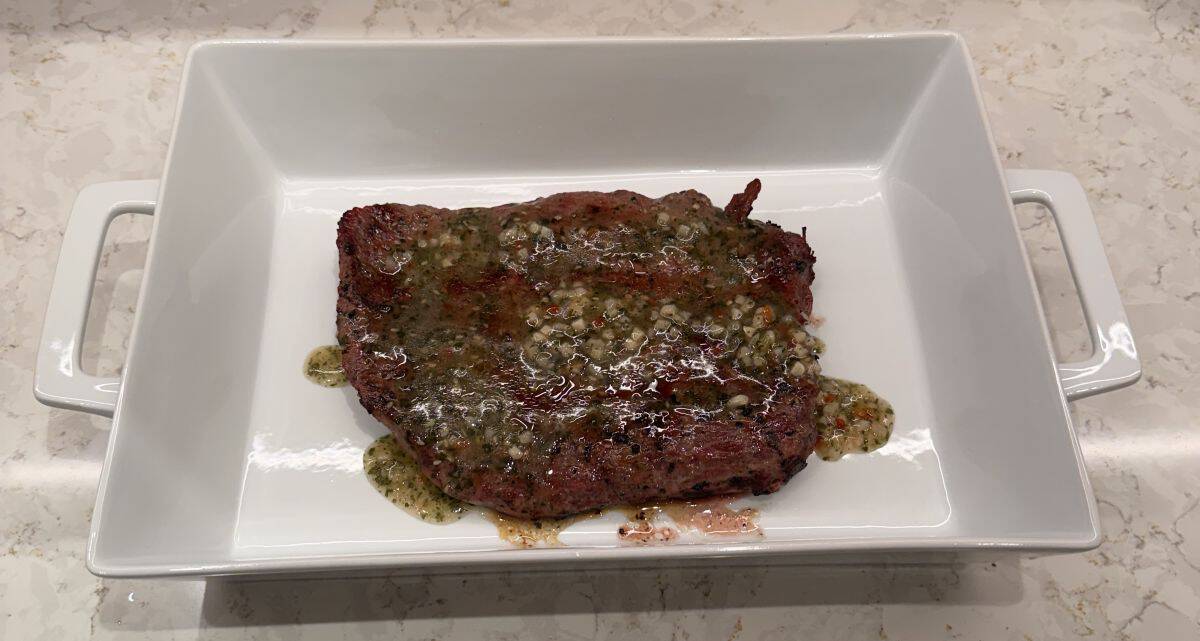 Top down image of the entire flank steak cooked and sitting in a glass dish with marinade on top.