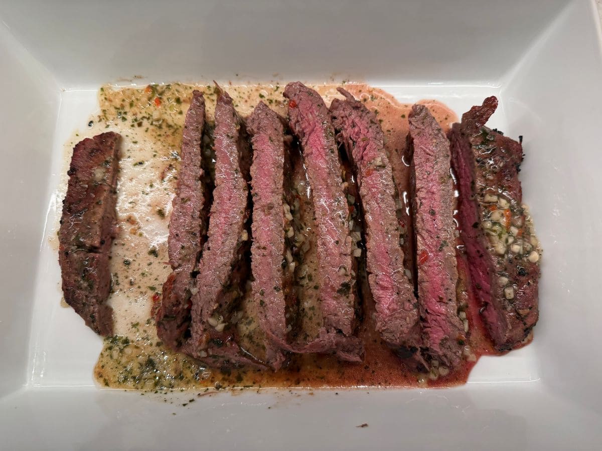 Image of the steak after being cooked and sliced in a white serving dish.