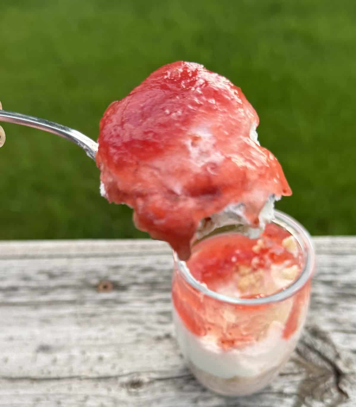 Closeup image of a spoon with strawberry shortcake mousse on hovering over a glass container with mousse.