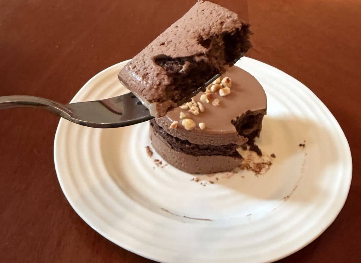 Image of fork hovering over a plate with a hazelnut mousse cake, there's a bit of cake on the fork.