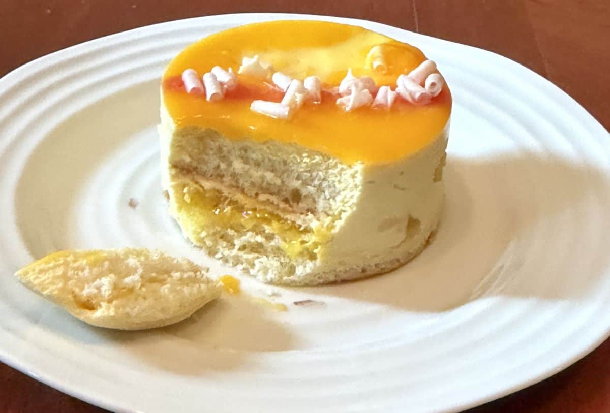 Image of a tropical mousse cake served on a white plate with a bit taken out of it so you can see the center.
