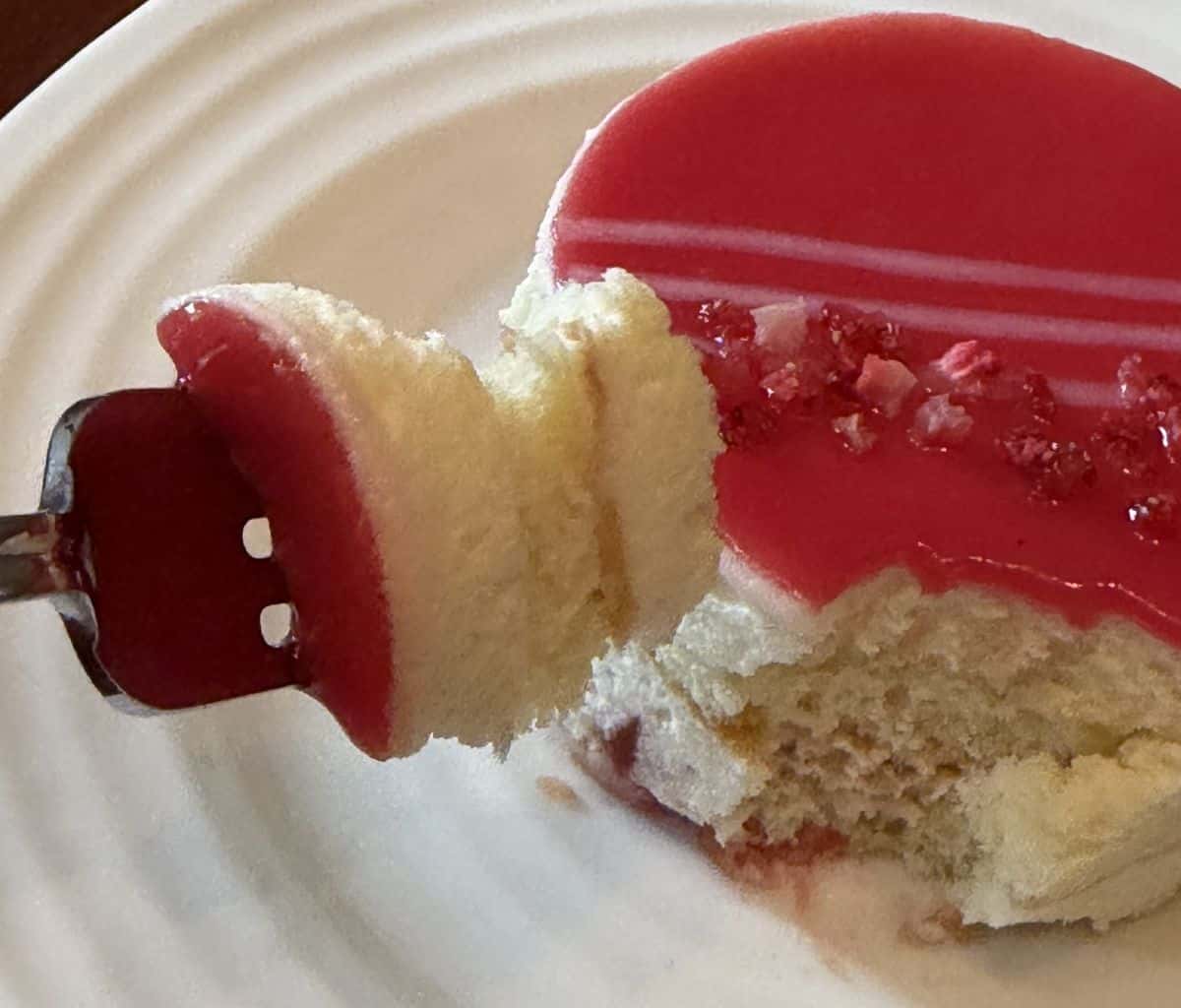 Image of a white chocolate strawberry mousse cake with a bite taken out if so you can see the center of the cake.