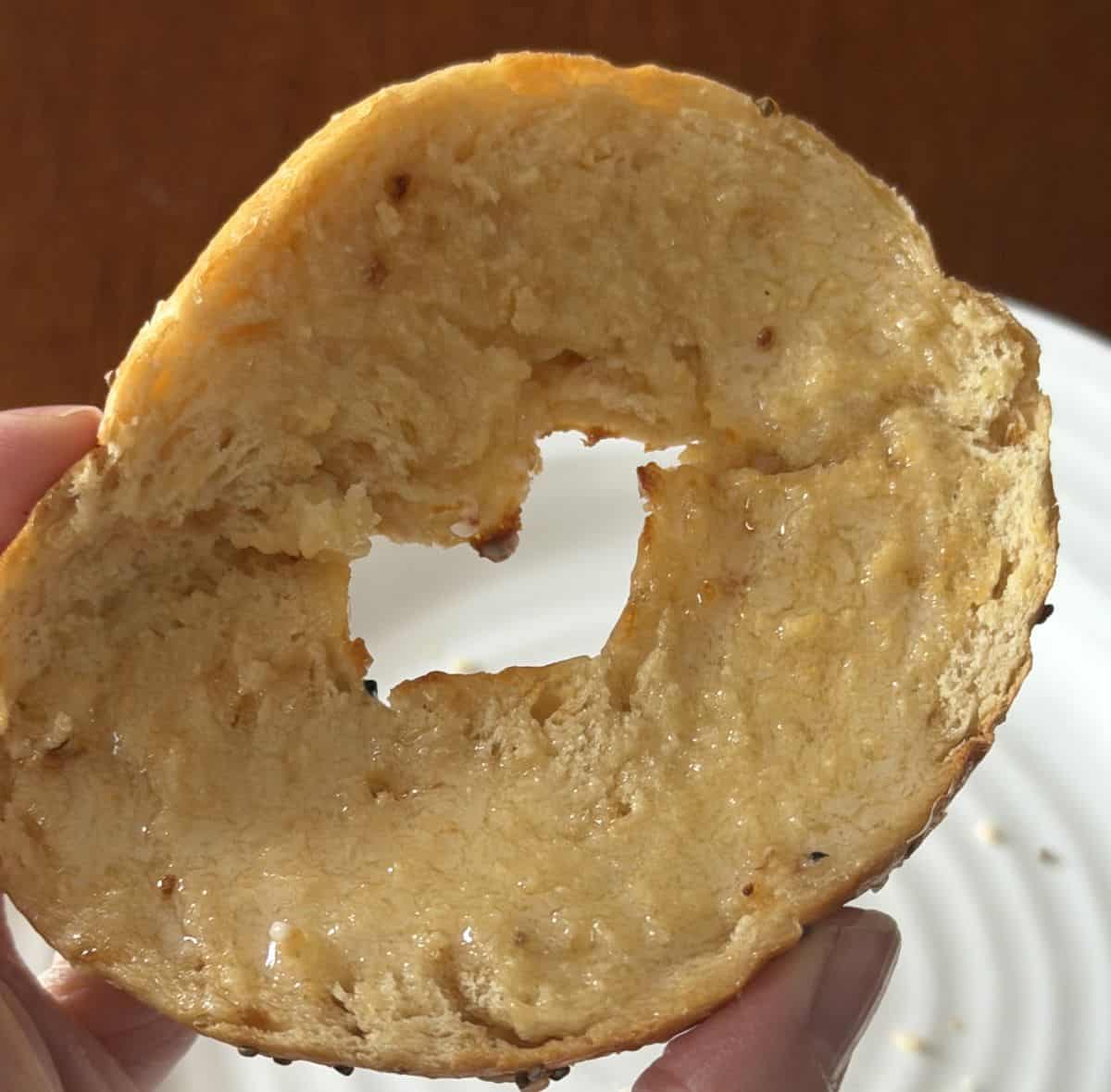Image of a hand holding half a bagel close to the camera that's been toasted and has butter on it.
