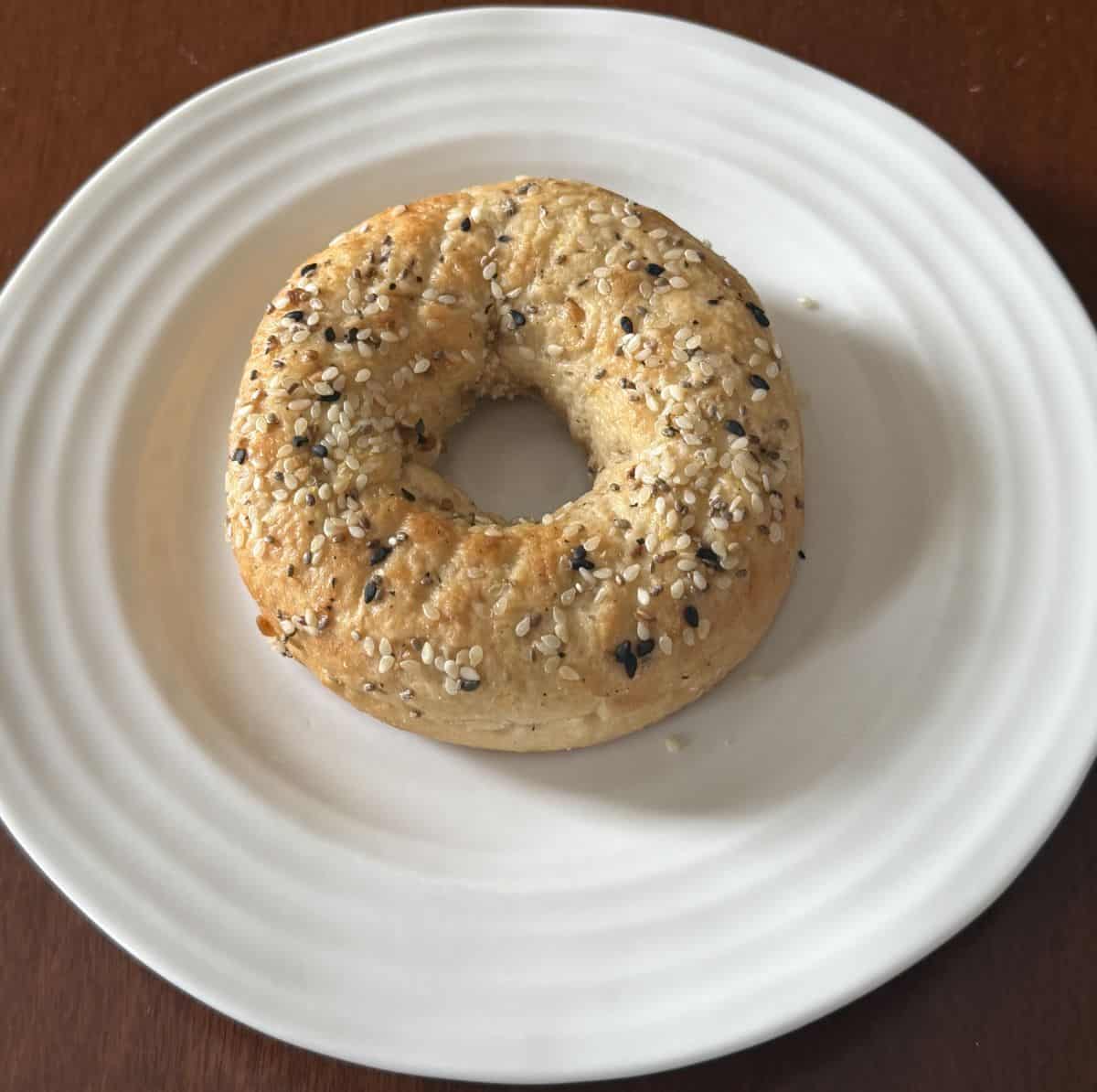 Image of one protein bagel served on a white plate. The bagel is not cut or toasted.
