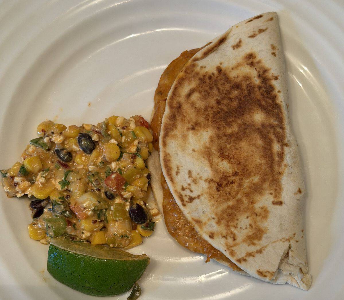 Closeup top down image of one cooked quesadilla beside a side of corn salad.
