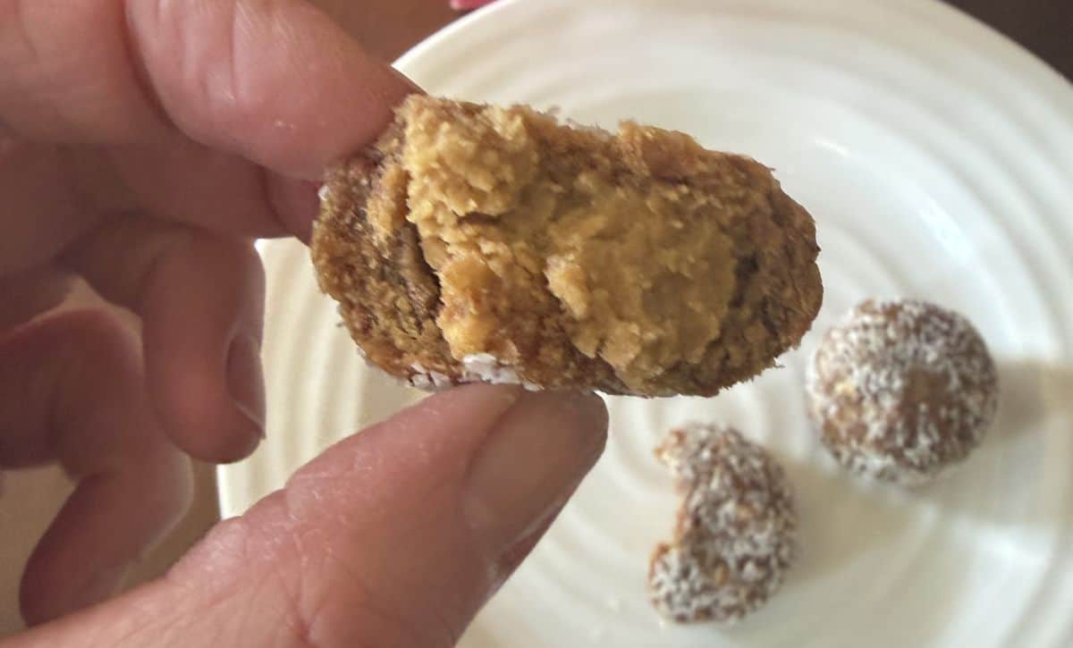 Image of a hand holding one energy bite close to the camera with a bite taken out of it so you can see the peanut butter inside,