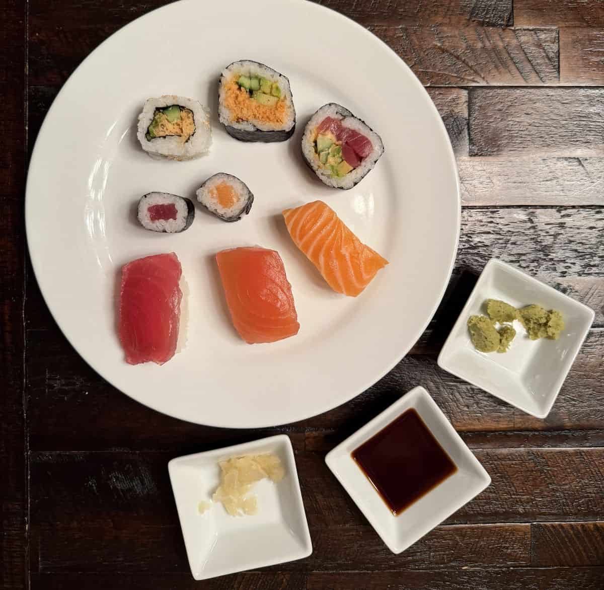 Image of pieces of nigiri, maki, spicy crab roll, spicy tuna roll and maki served on a white plate.
