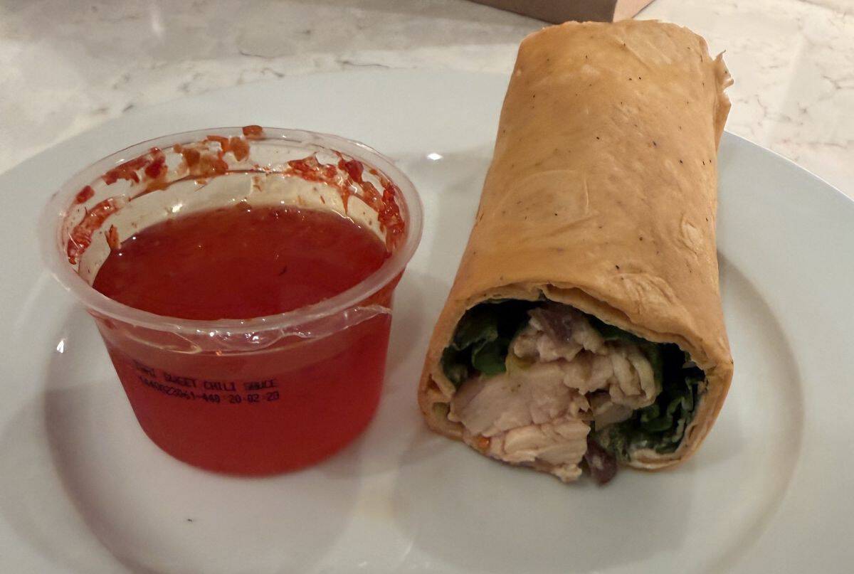 Image of a wrap served on a white plate beside a container of sweet chili sauce.