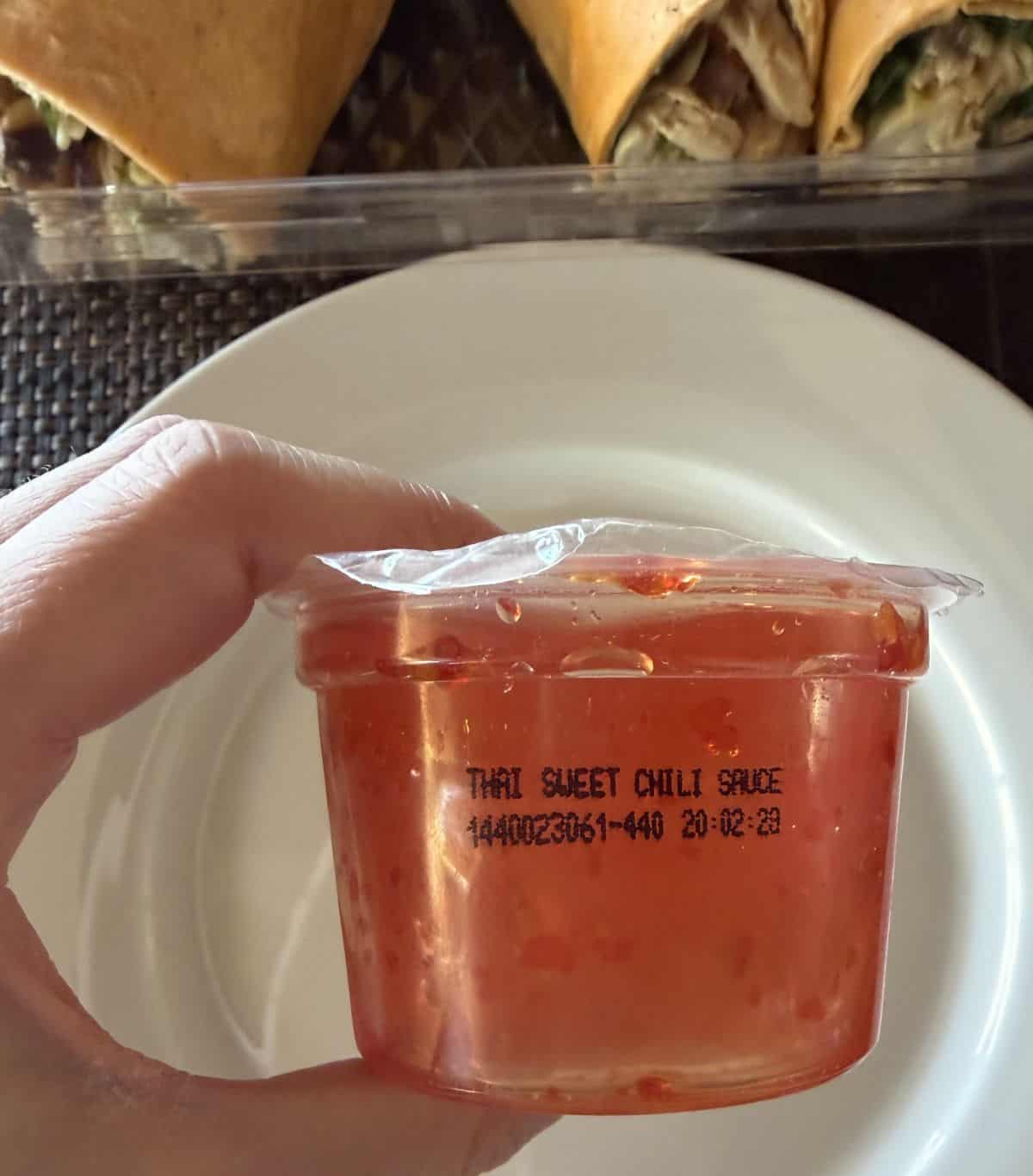 Image of a hand holding a sweet chili sauce container that's unopened close to the camera.