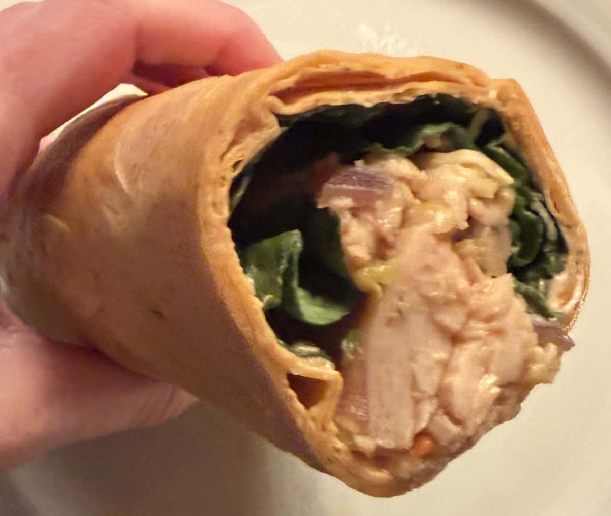 Closeup image of a hand holding a wrap close to the camera so you can see the filling inside.