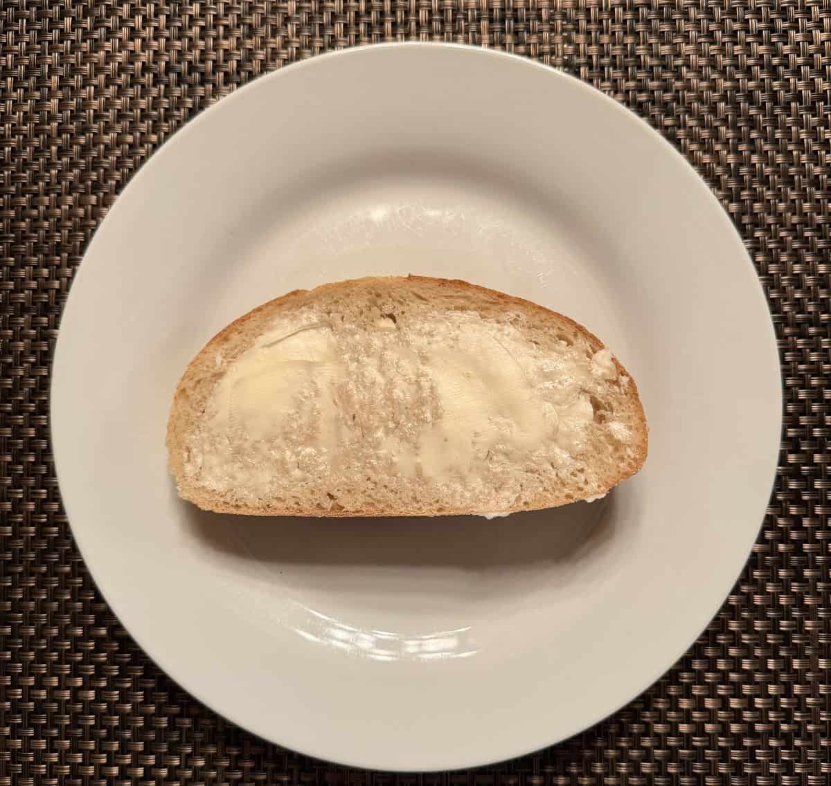 Image of a piece of bread served on a white plate with butter spread on it.