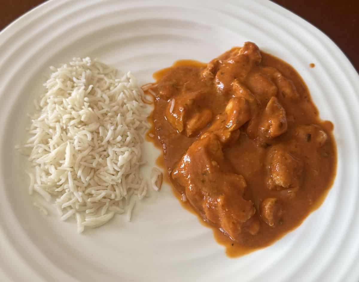 Top down image of the heated butter chicken beside a side of rice on a white plate.