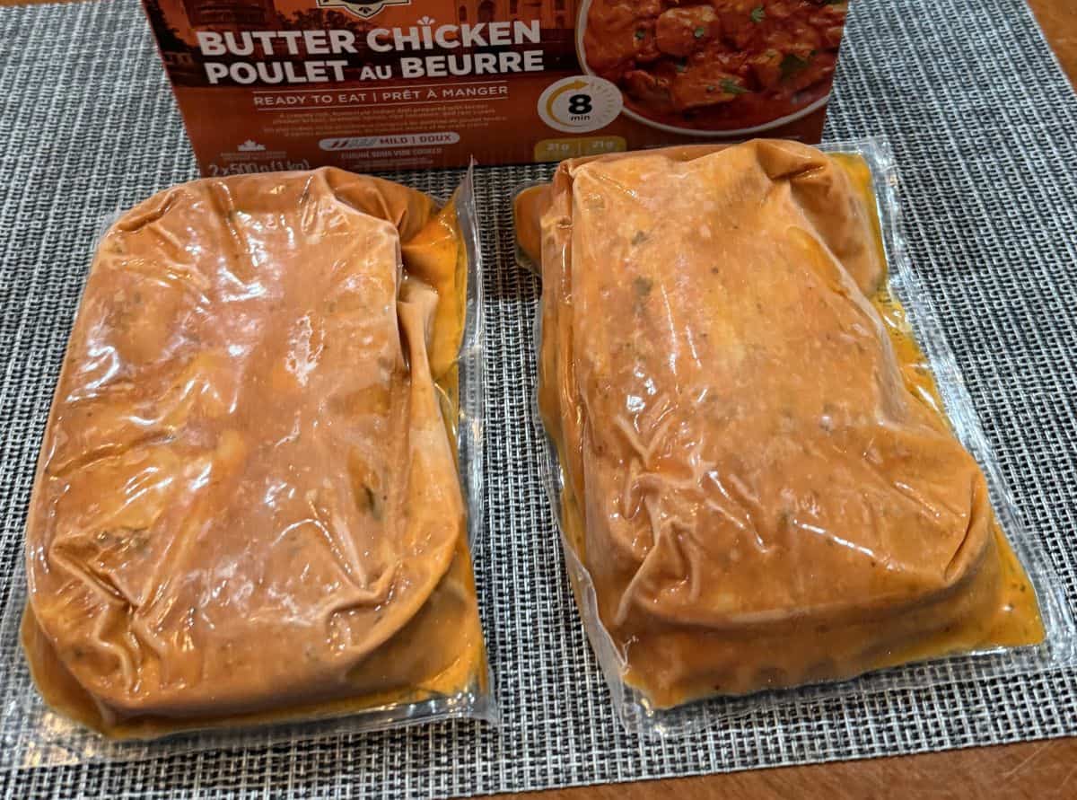 Image of two unopened vacuum sealed packs of butter chicken sitting in front of the box of butter chicken.
