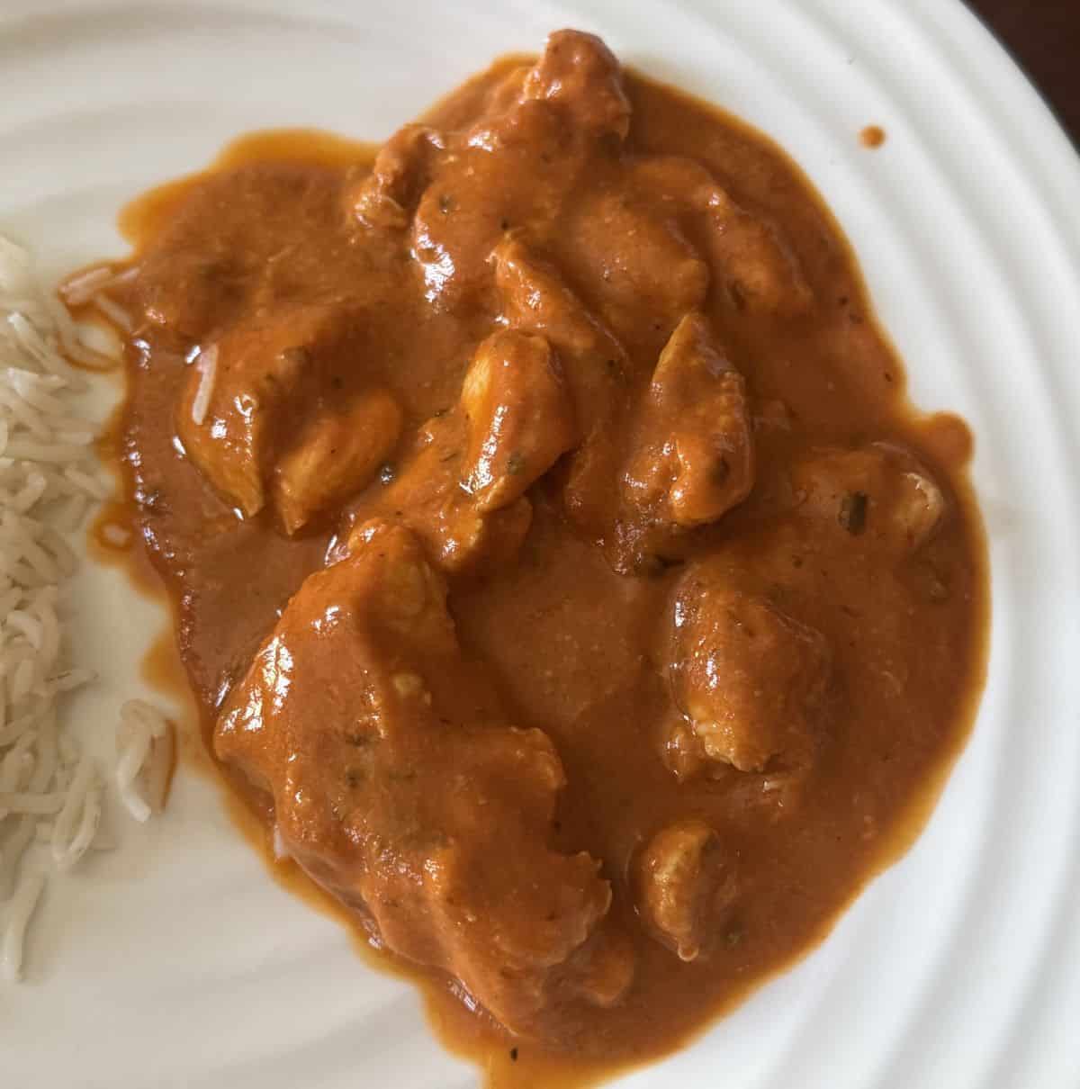 Top down image of the butter chicken served on a white plate.
