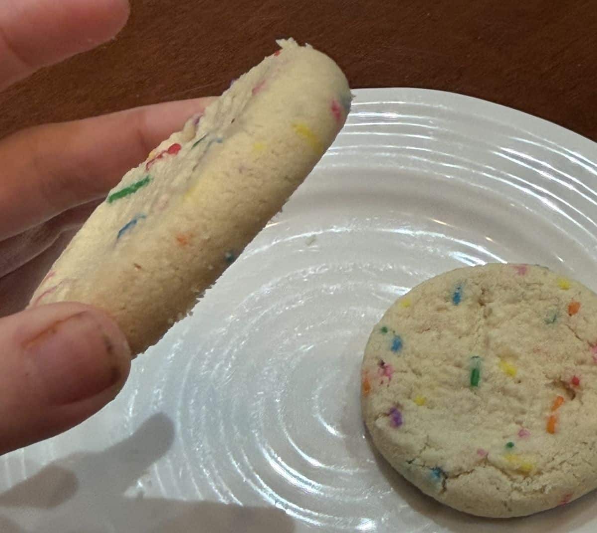 Image of a hand holding one cookie near the camera on its side so you can see how thick the cookie is.