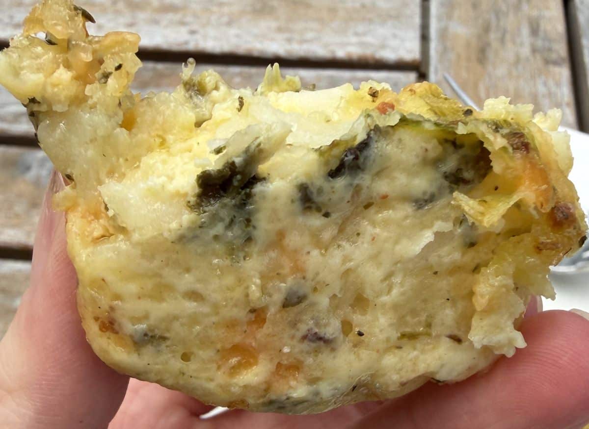 Image of a hand holding one potato egg bake close to the camera so you can see the inside.