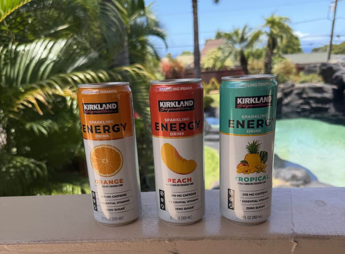 Image of three cans of energy drinks in different flavors unopened sitting on a deck in front of a pool.
