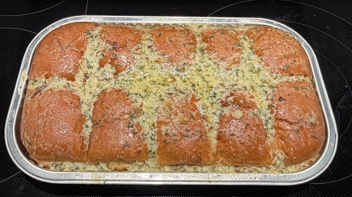 Image of the Costco Kirkland Signature Brioche Garlic Bread without the lid after being heated in the tray and sitting on a stovetop.
