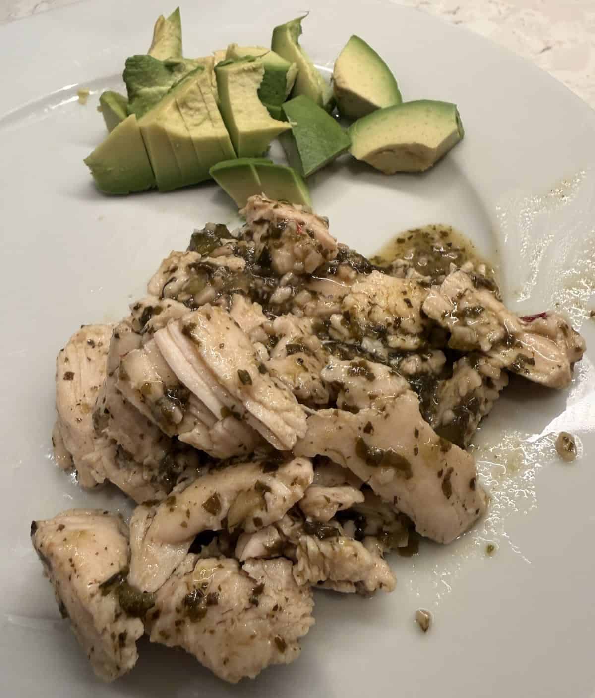 Image of the chicken served on a white plate beside some avocado.