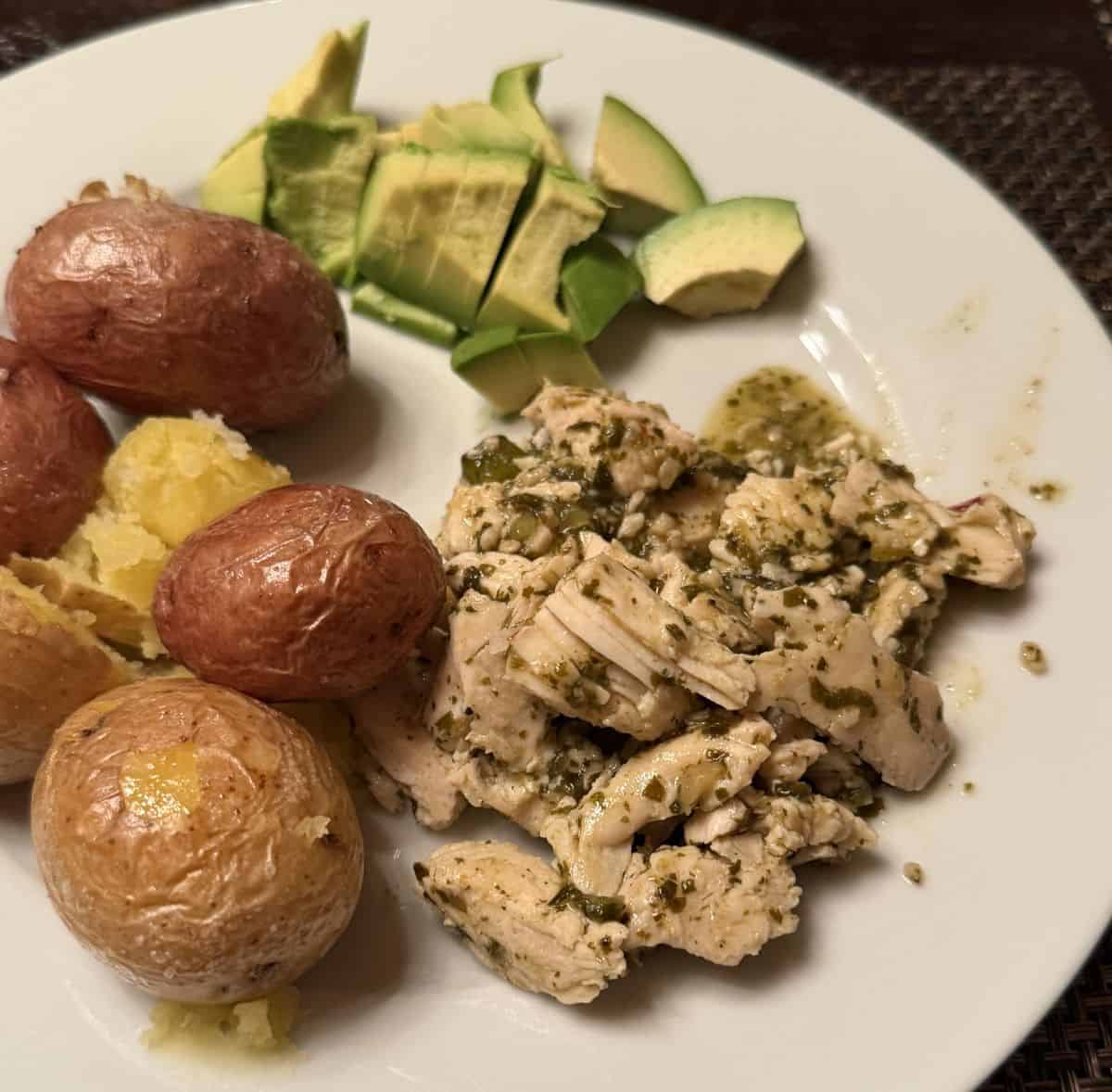 Image of the chicken served on a white plate beside potatoes and avocado.