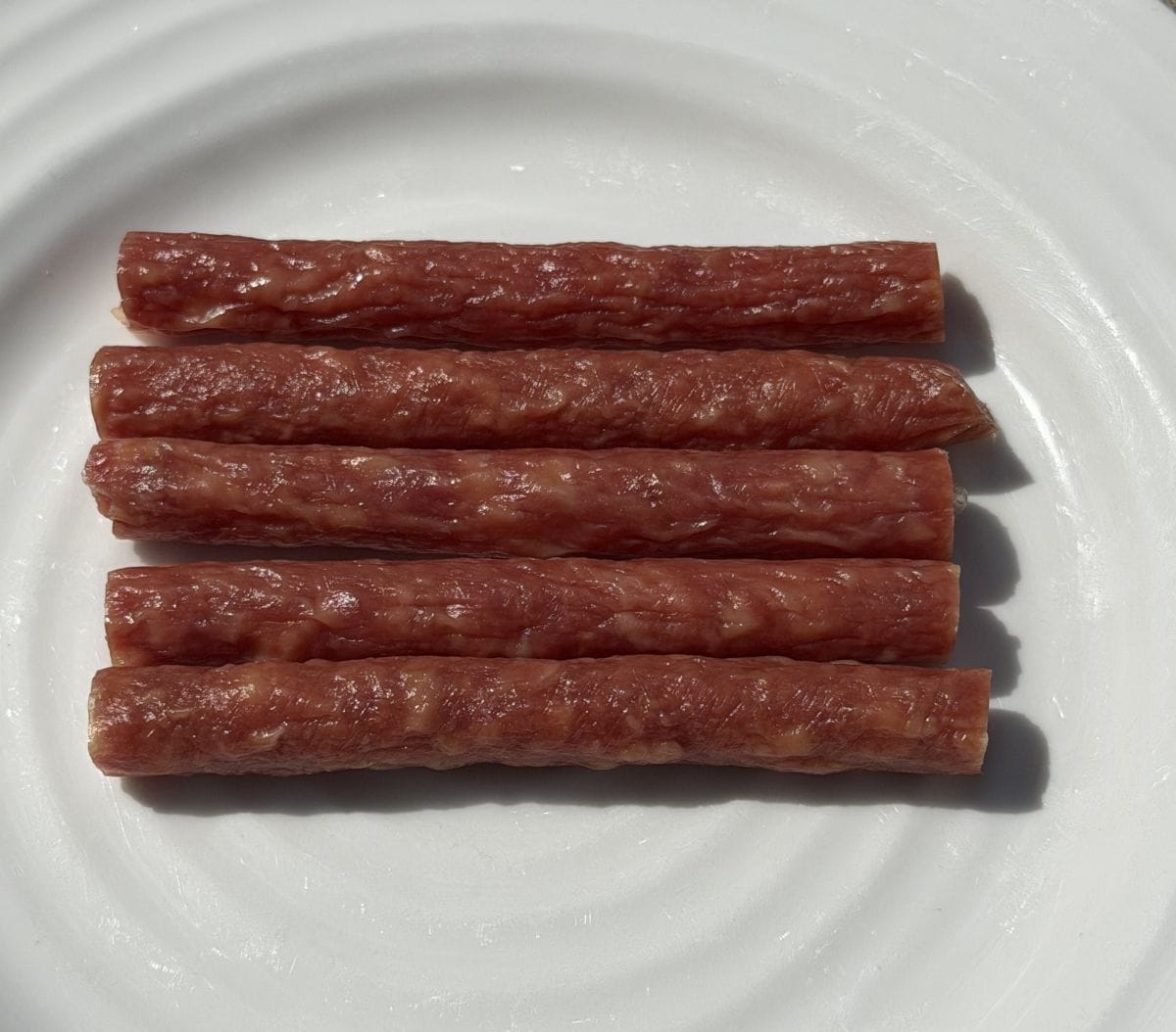 Top down image of five salami sticks sitting on a white plate.