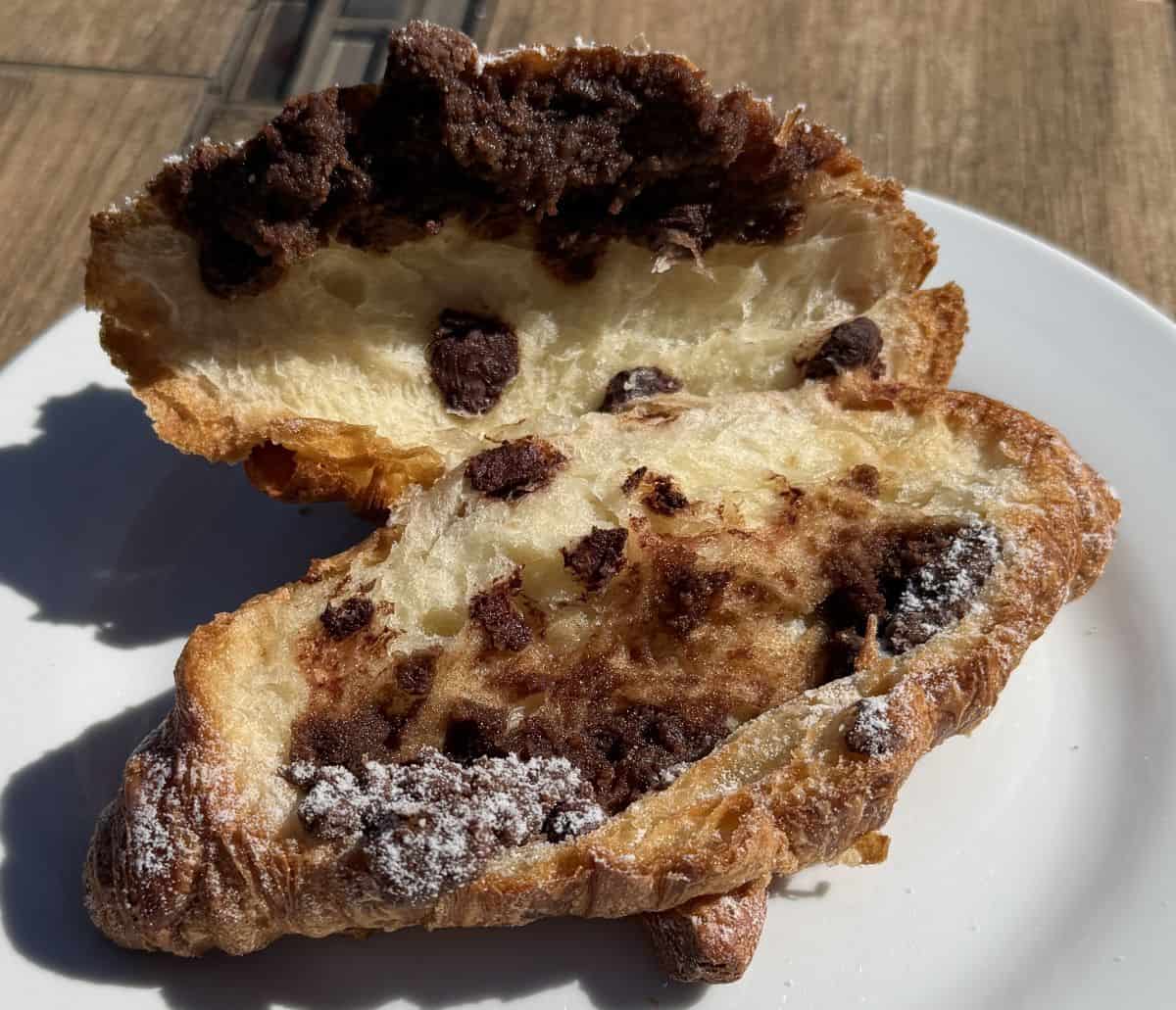 Image of one Twice Baked Chocolate Filled Croissant served on a white plate and cut in half so you can see the chocolate inside.