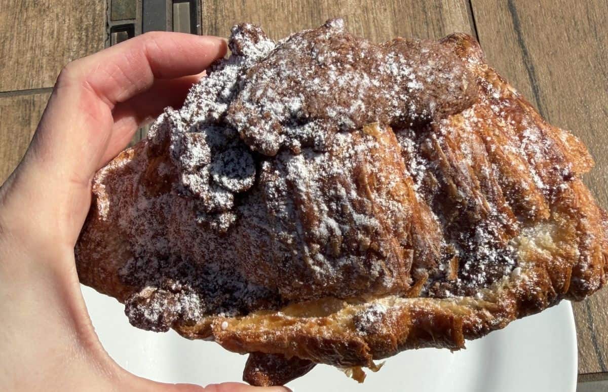 Closeup image of a hand holding one twice baked chocolate filled croissant close to the camera.