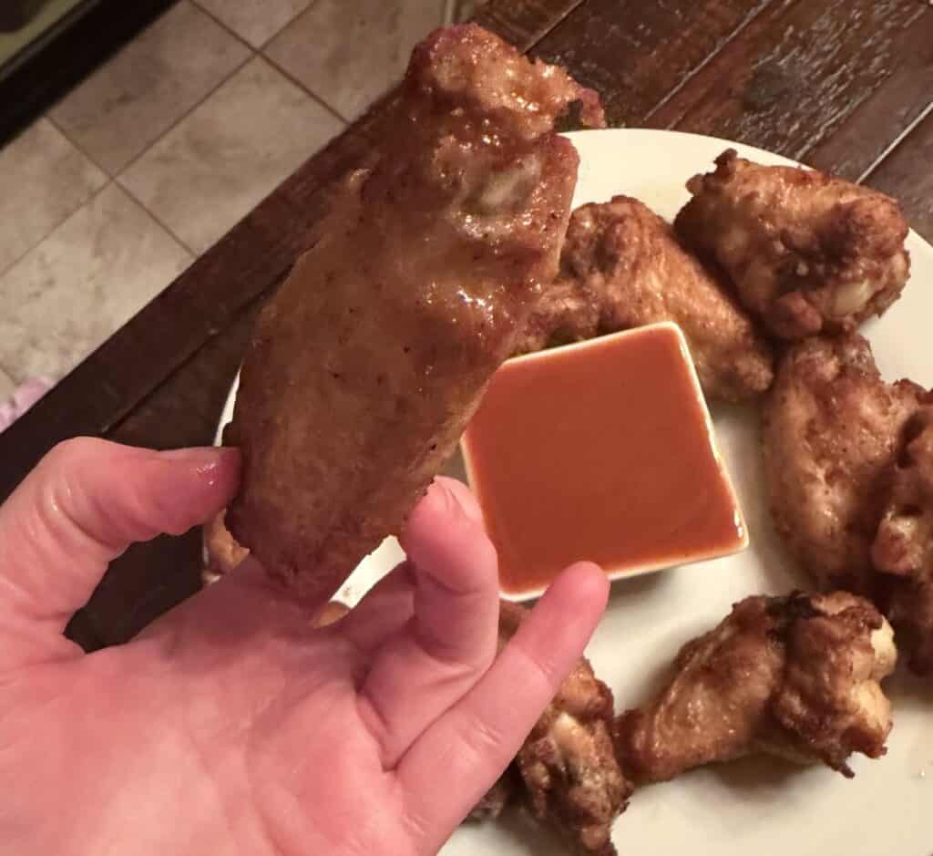 Image of a hand holding one drumstick wing, close to the camera, hovering over a plate of wings.