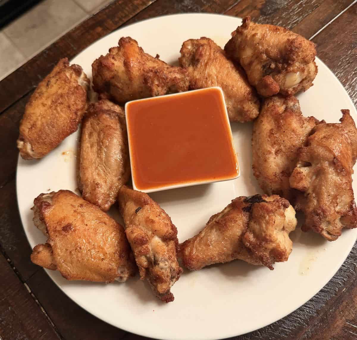 Top down image of the wings cooked and served on a white pate with buffalo sauce in the middle.