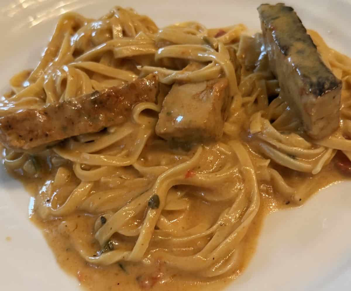 Closeup top down image of the linguine, chicken and sausage cooked and served on a white plate.